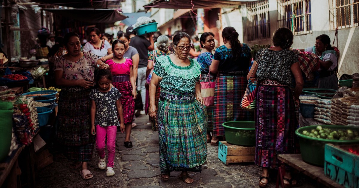 Women and children in colorful traditional dresses at a bustling Guatemalan market.