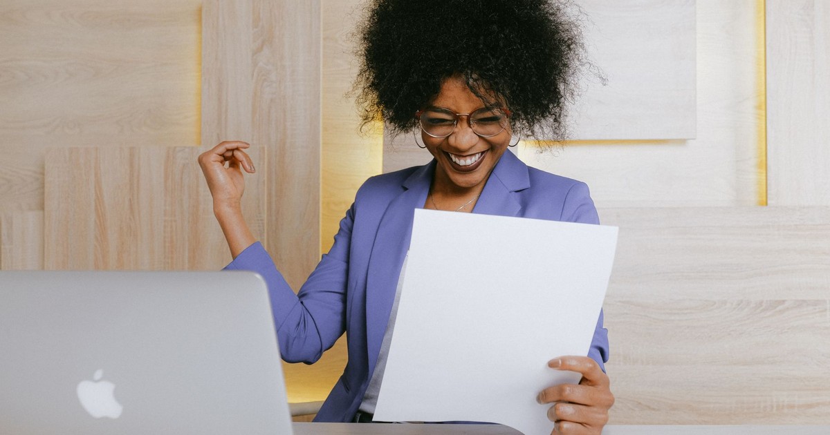 A cheerful woman celebrates her success at work, looking at a document in an office setting.