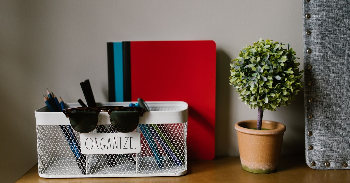 A tidy workspace featuring a basket with stationery, a mini tree, and a colorful notebook.