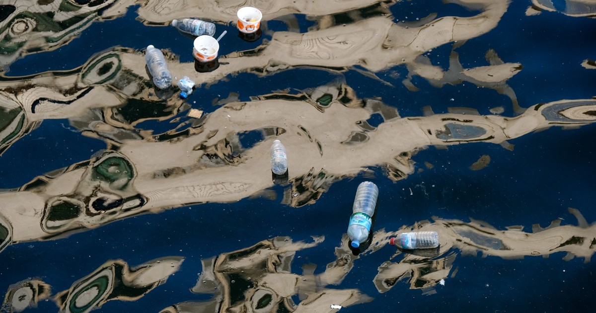 Floating plastic bottles and trash polluting a waterway with reflections.