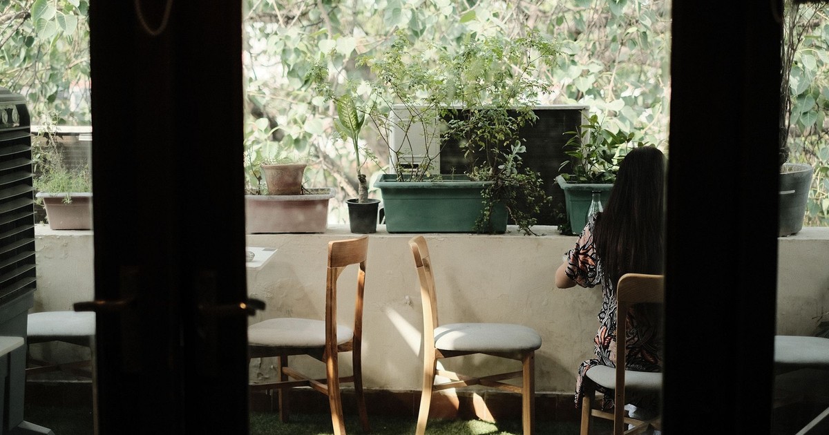 A serene balcony view featuring a woman sitting amidst potted plants and chairs.