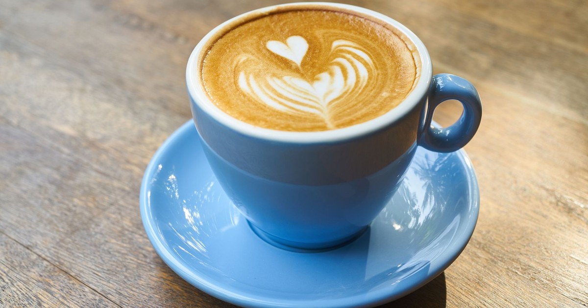 A beautifully crafted latte with heart-shaped art in a blue cup on a wooden table.