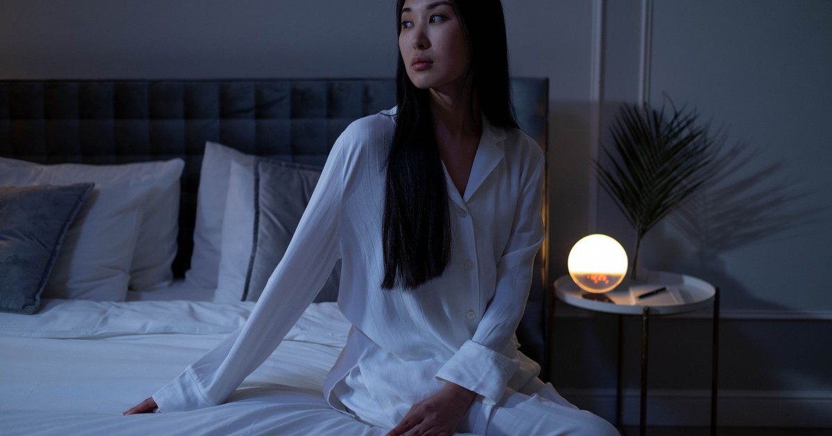 Woman in white pajamas sitting on a bed with warm lighting, showcasing a calm evening indoors.