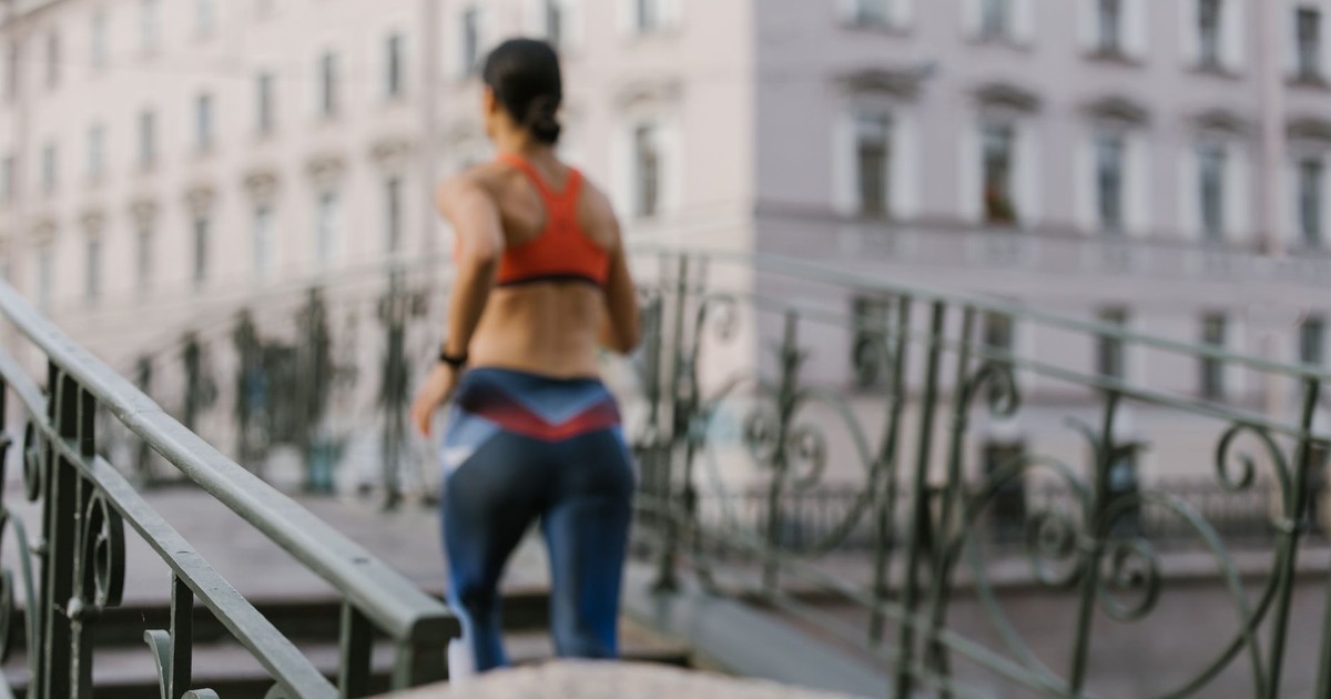 A woman in activewear jogs on a city bridge, focusing on health and fitness lifestyle.