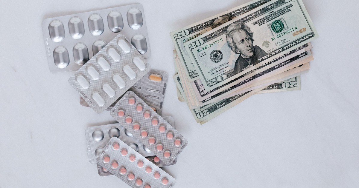 From above of silver blister full of drug near big pile of dollar to spend on medication