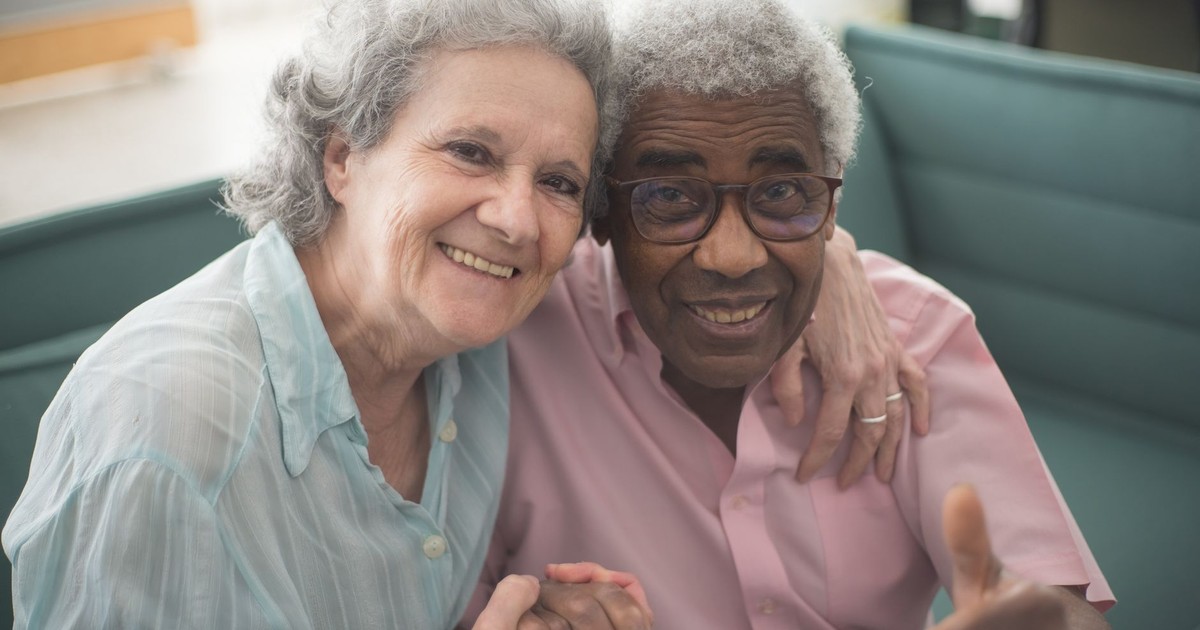 Elderly couple sharing a joyful moment indoors, sitting together on a couch with loving expressions.