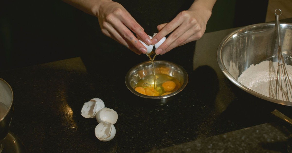 Hands cracking eggs into a bowl, with flour ready for baking. Perfect for culinary scenes.