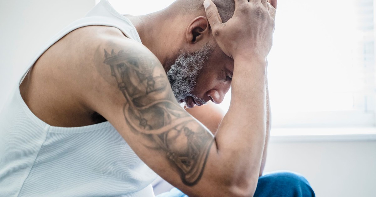 Side view of a thoughtful bald man with an arm tattoo, sitting indoors.