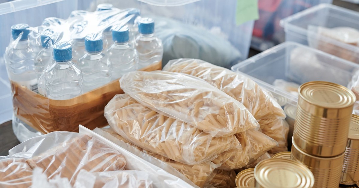 Plastic-wrapped food items and bottled water organized in storage containers and tin cans.