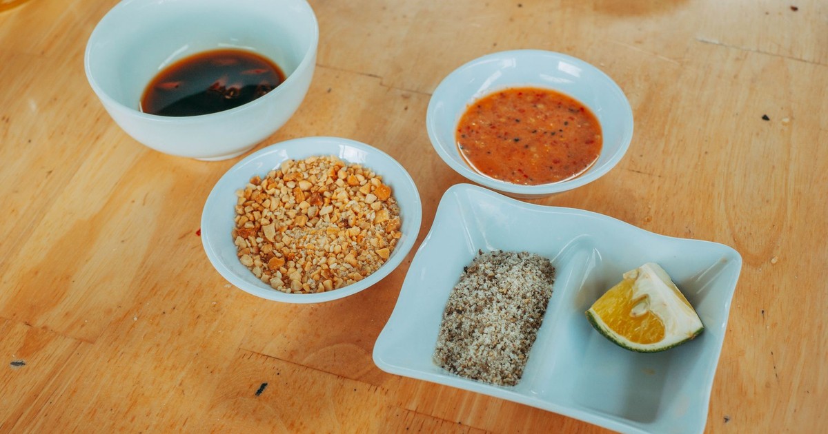 Variety of condiments including lime, peanuts, and sauces on a wooden table.