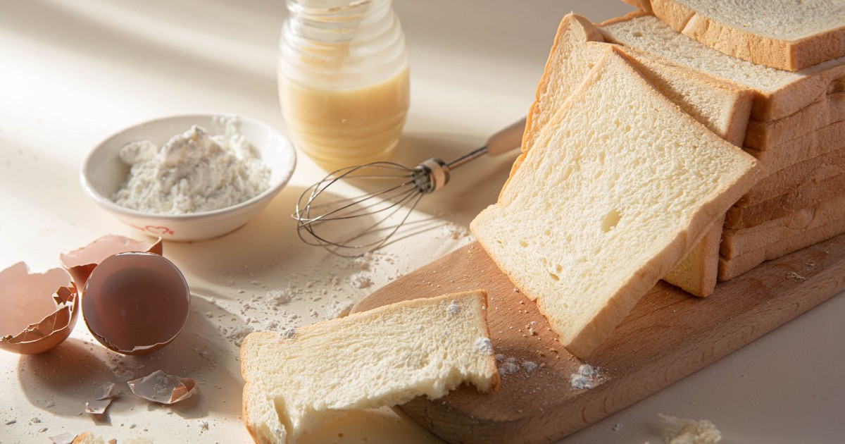 Sliced bread with flour, egg, and whisk on a wooden board, perfect for baking themes.