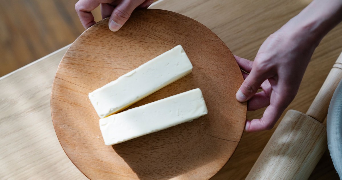 Close-up of hands holding a wooden plate with two butter sticks. Ideal for food and culinary themes.