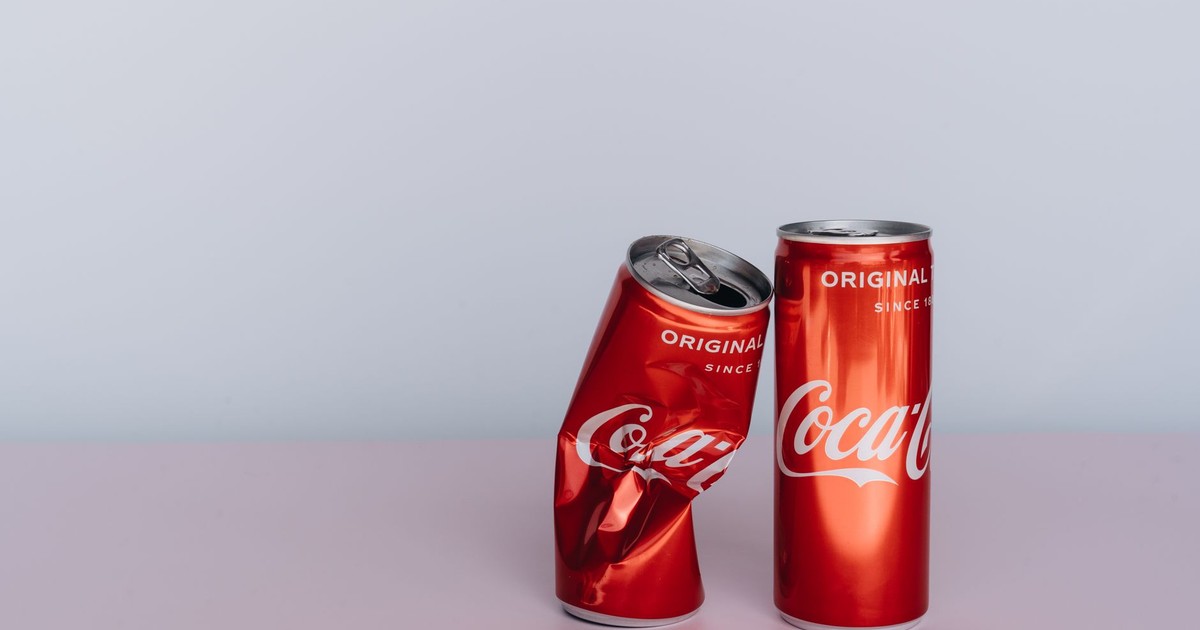 Two Coca Cola cans, one crumpled, on a minimalist tabletop with ample copy space.