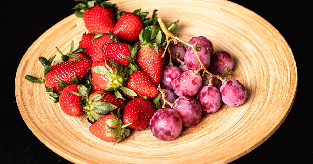 A vibrant display of fresh red strawberries and purple grapes on a rustic wooden plate.