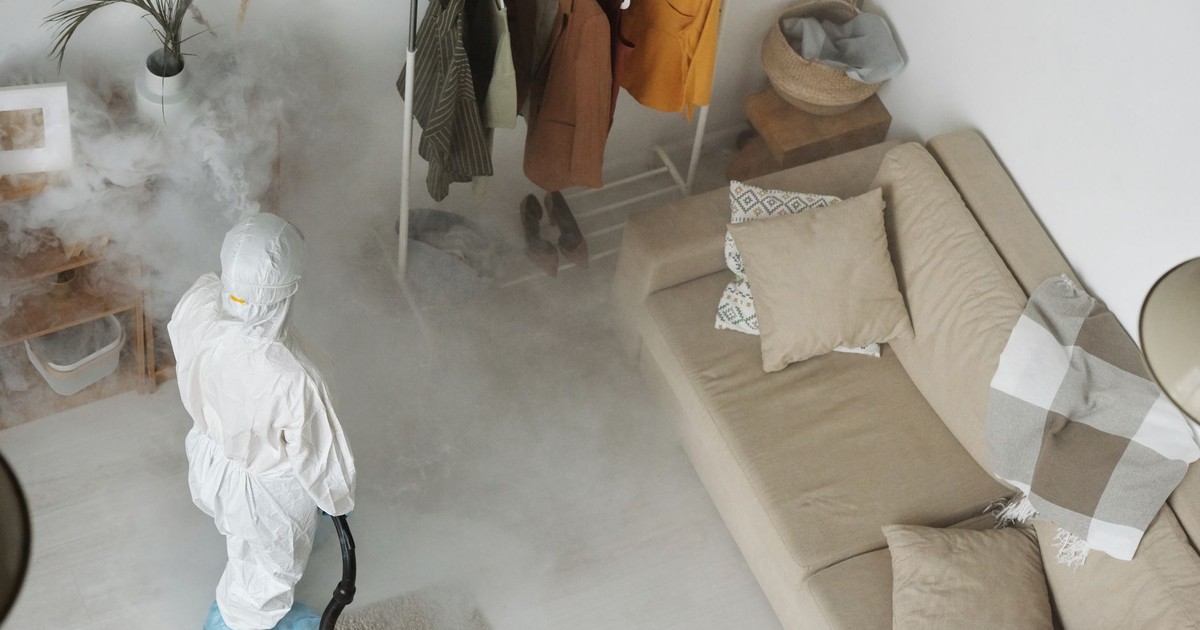 Professional in protective gear sanitizing a modern living room with a fumigation machine.