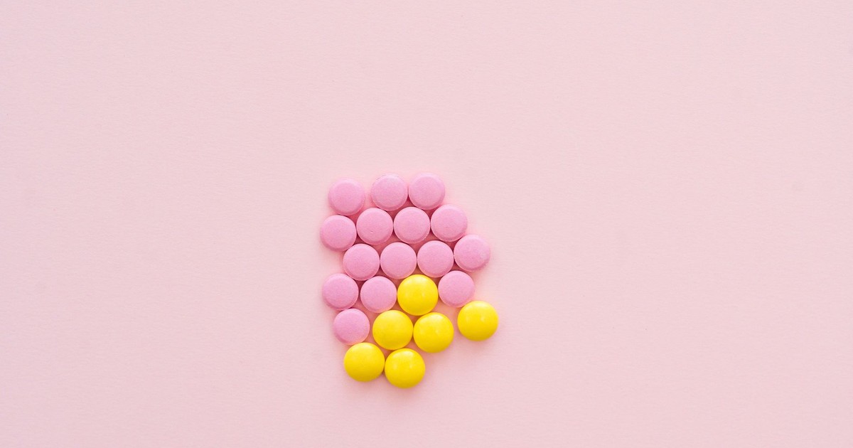 Pink and yellow pills arranged on a pastel pink background in a flat lay style.