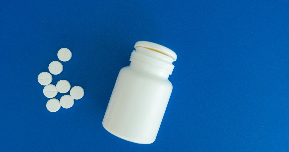 Flat lay of white pills and a container against blue backdrop, symbolizing healthcare.