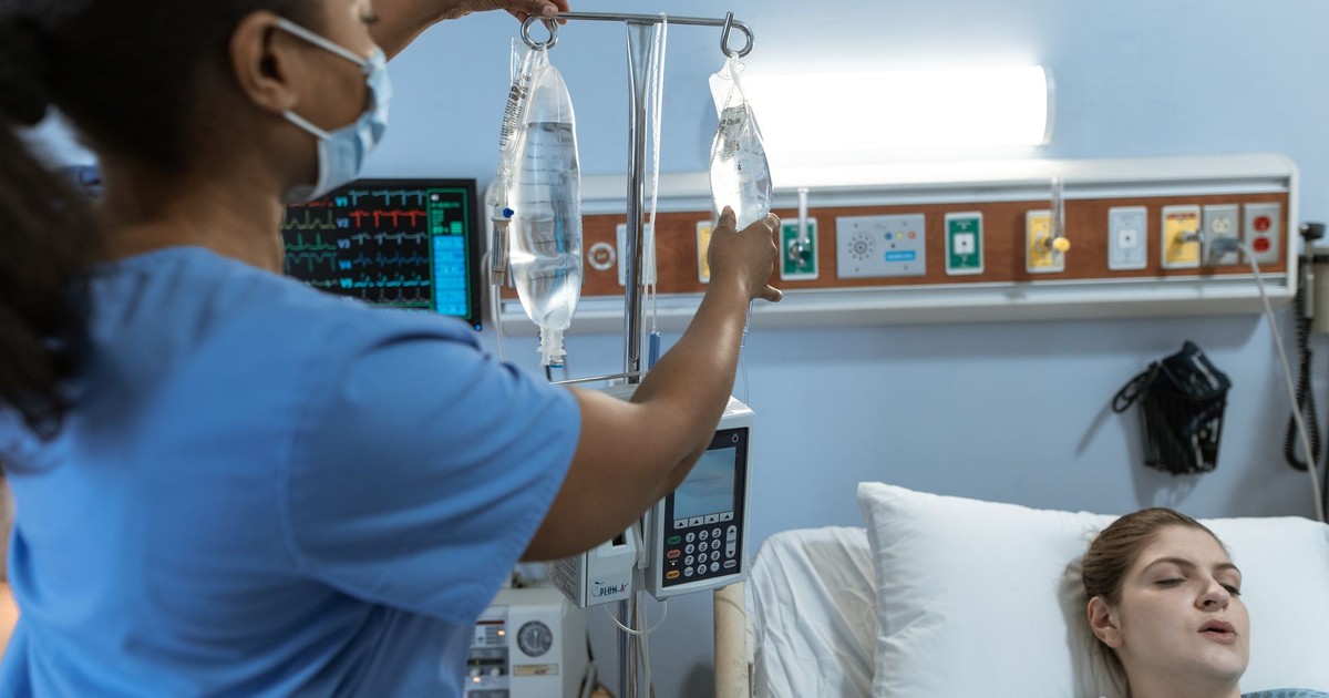 A nurse in a hospital setting adjusts an IV drip for a patient lying in bed, showcasing medical care.
