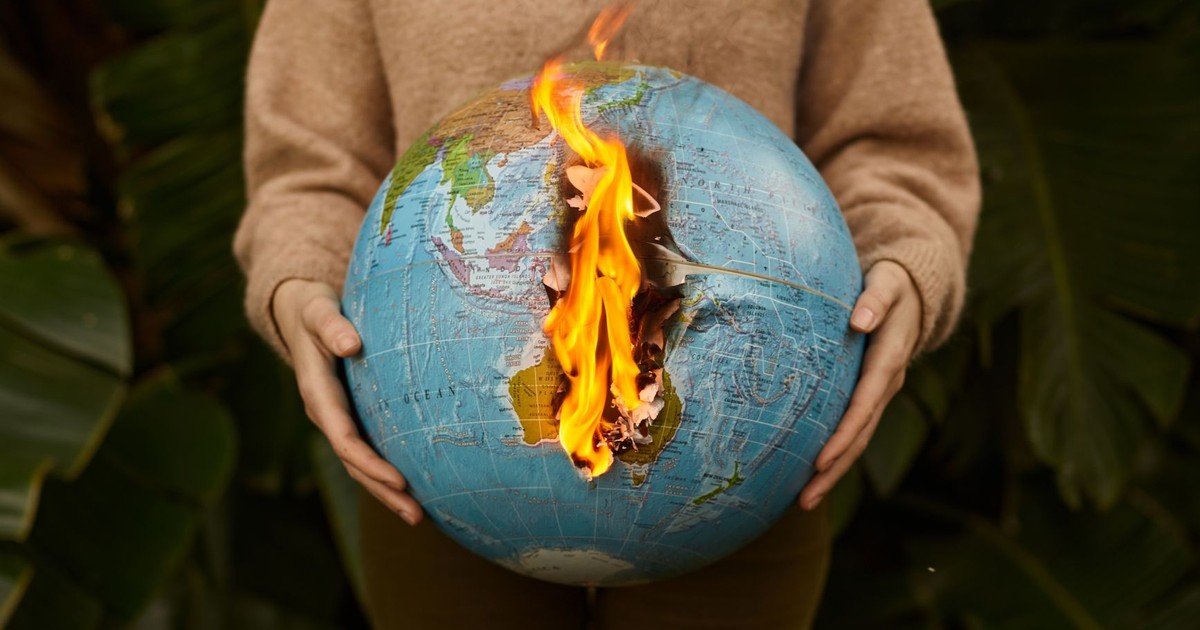 A symbolic portrayal of climate change with a burning globe held in hands, set against a nature background.