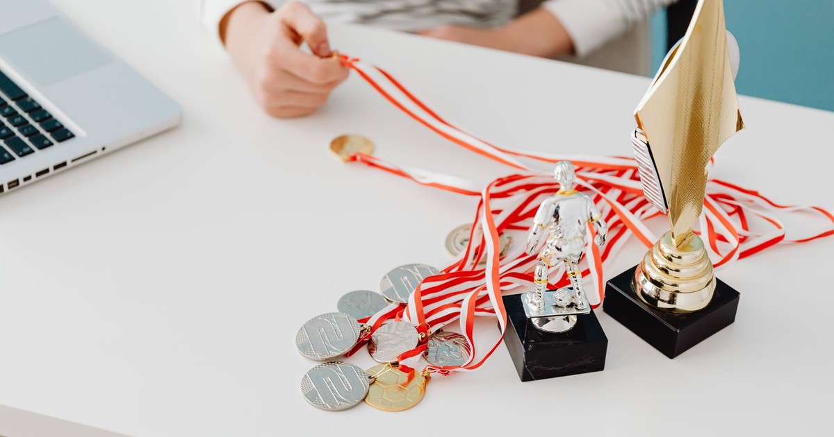 Young person displays football trophies and medals on a desk, showcasing athletic pride.