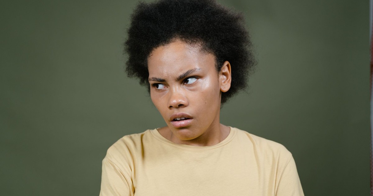 Close-up of a young woman with afro expressing a pensive mood against a green background.