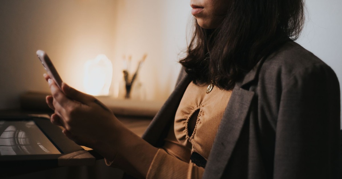 A stylish woman using a smartphone in an intimate home office, wearing a suit jacket.