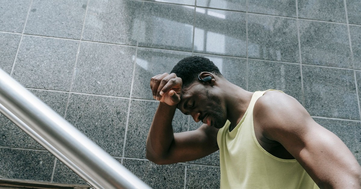A tired black man resting on stairs in a modern building, reflecting fatigue and effort.