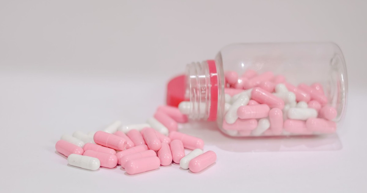 Close-up of pink and white capsules spilled from a plastic bottle on a white background.
