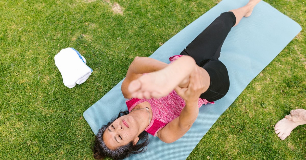 Senior woman stretching on a yoga mat in a park, embracing outdoor wellness and fitness.