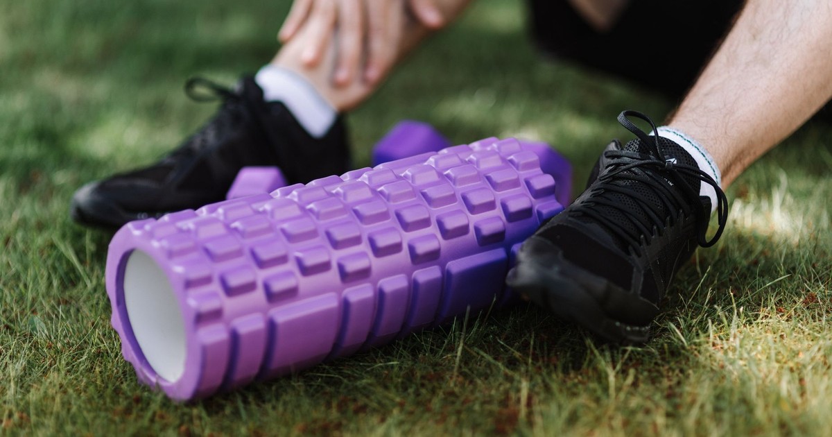 Black sneakers and purple foam roller on grass, outdoor fitness scene.