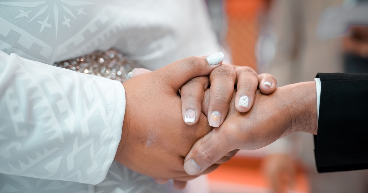 Detailed close-up of a bride and groom holding hands during their wedding ceremony.