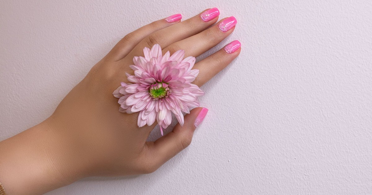 Close-up of a woman's hand with pink nails and a pink flower, showcasing delicate beauty.