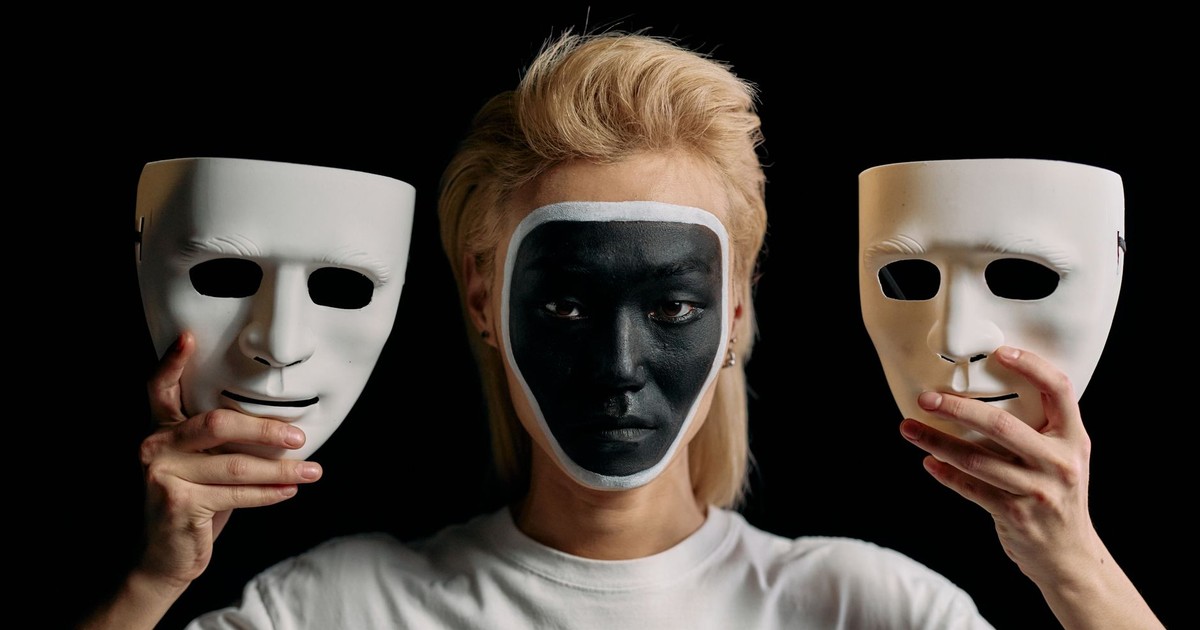 A conceptual portrait featuring art makeup with mask elements on a plain black background.