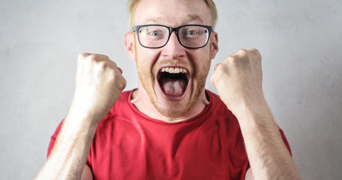 A cheerful man in a red shirt expressing excitement indoors.