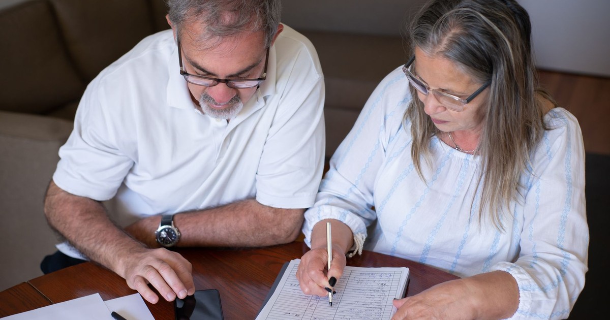 Elderly couple reviewing documents, using smartphone for online banking at home.