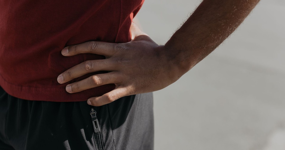 Close-up image of a hand resting on the waist, wearing a red shirt and black pants.
