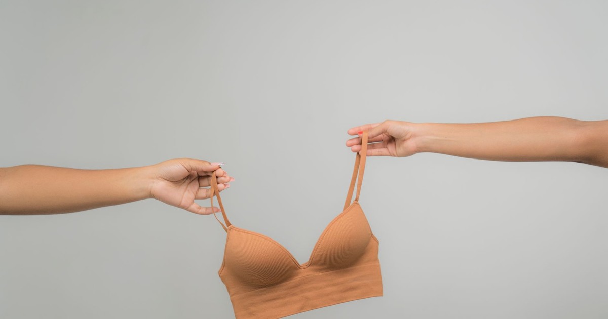 Two hands holding a nude bra against a light, neutral background, emphasizing fabric texture and design.