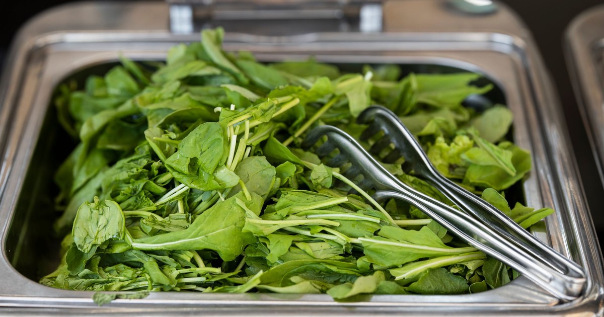 Close-up of fresh green vegetables in a serving tray with metal tongs, ideal for healthy food concepts.