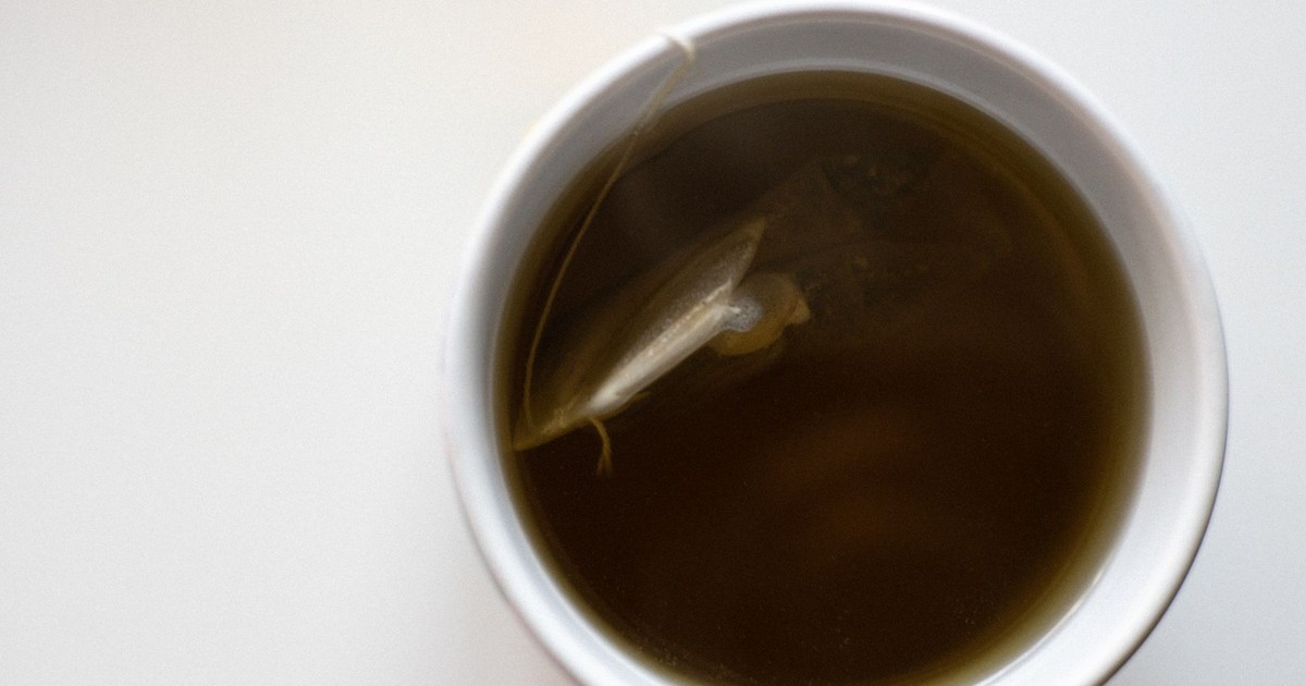 Top view of a white cup filled with fresh brewed green tea on a white background.