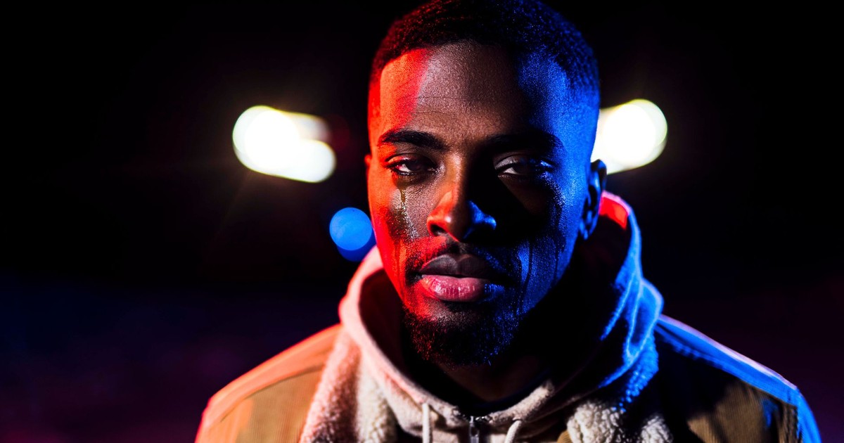 A dramatic portrait of a bearded man with tears, illuminated by colorful lights.