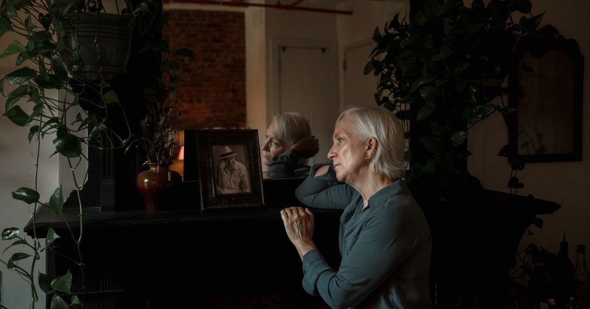 Elderly woman reflecting beside a photo frame and indoor plants.
