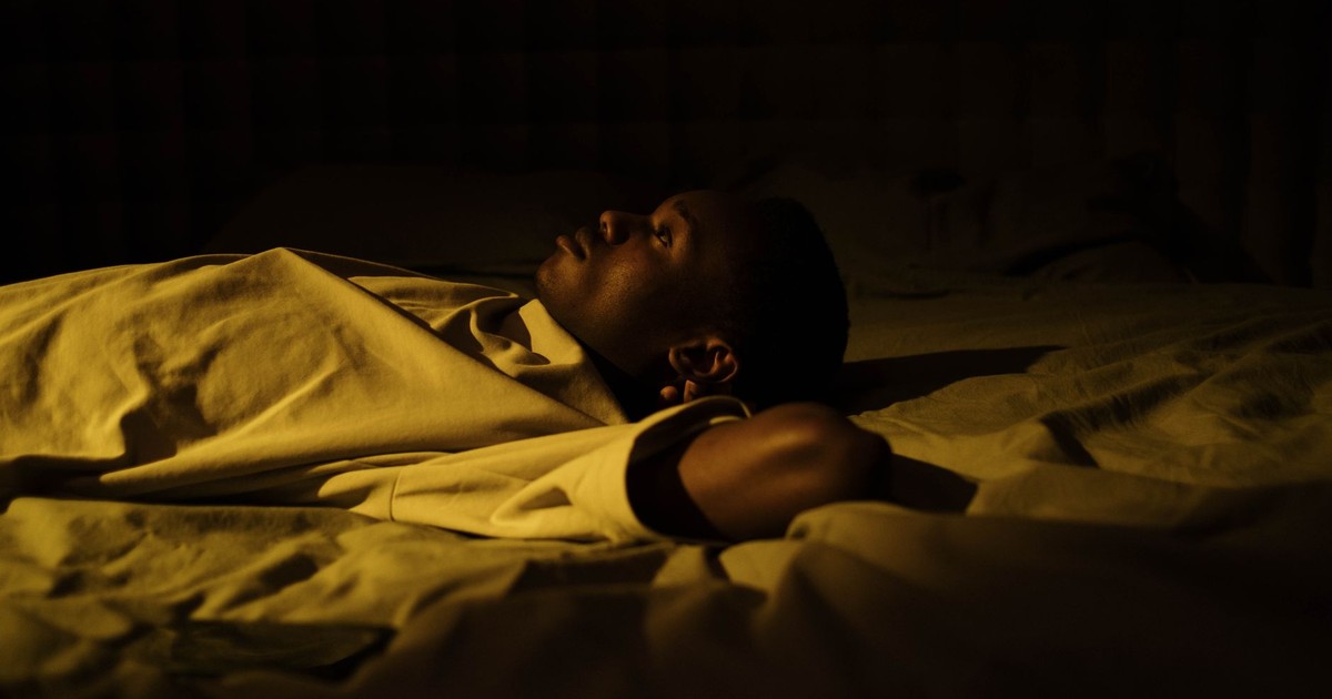 A man struggles with insomnia, lying awake in his dark bedroom at night, reflecting on mental health.