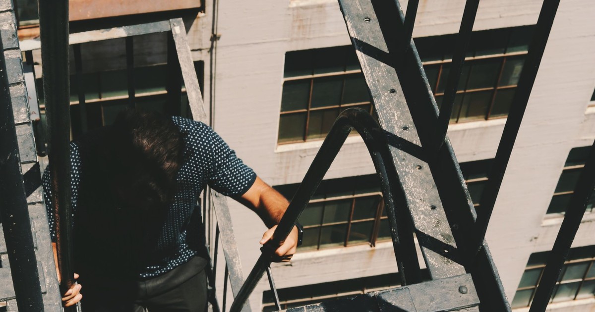A man climbing a fire escape on a city building on a sunny day.