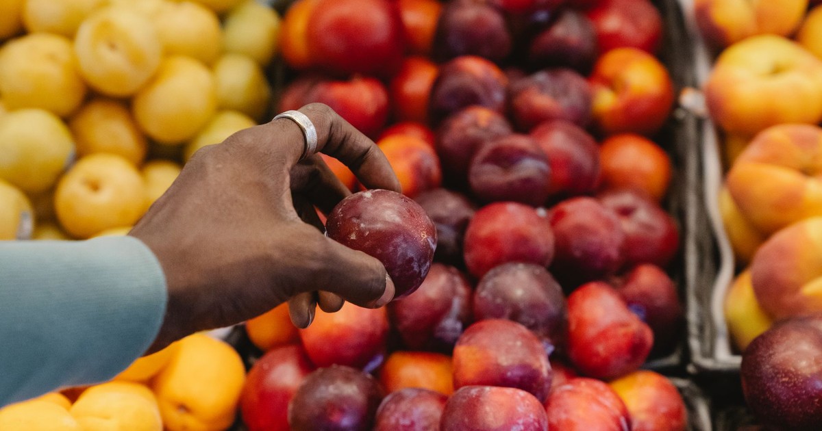 A hand picking fresh plums at a fruit market, showcasing a variety of colorful fruits.