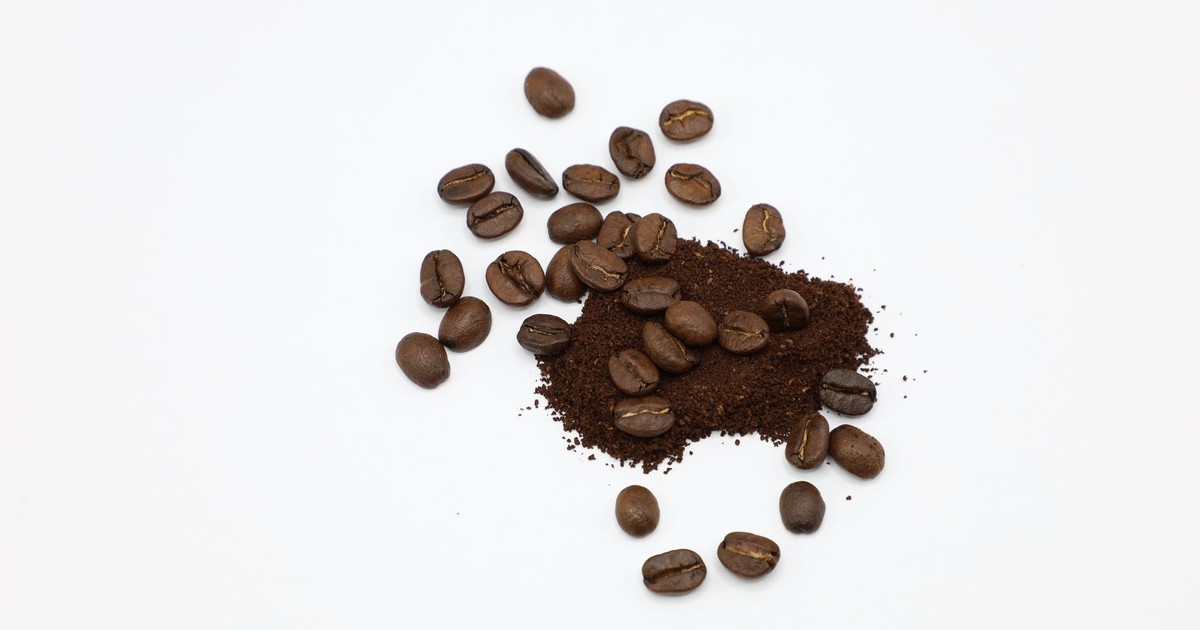 A detailed view of roasted coffee beans and ground coffee on a white surface, showcasing texture.