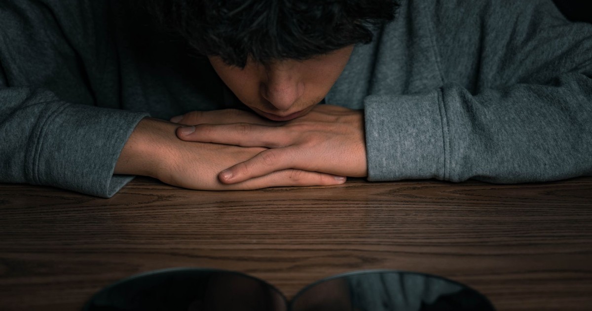 A young boy looking at his reflection in mirrors on a wooden table, deep in thought.