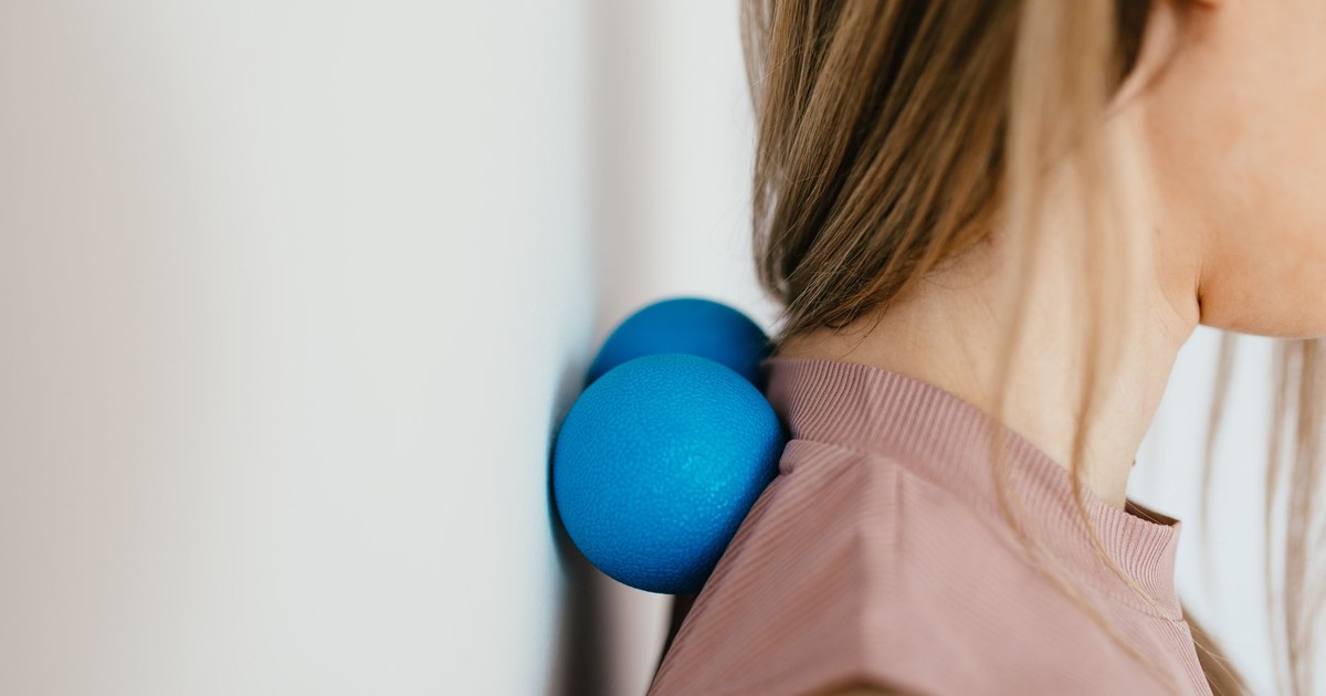 Side view crop unrecognizable female leaning on small balls against wall to massage stiff neck muscles and sore neck