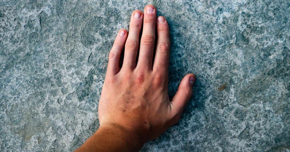 Close-up image of a human hand touching a rough textured stone surface.