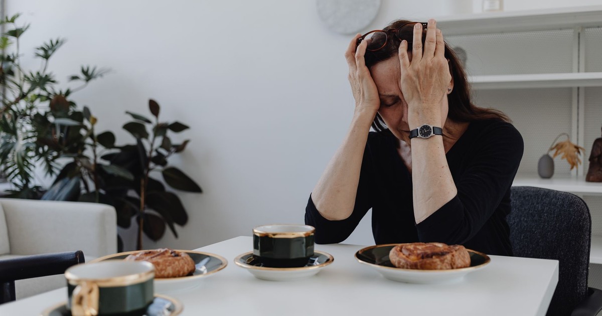 A woman in emotional distress sits at a table with coffee and pastries, illustrating loneliness and sadness.