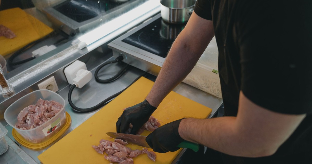 Man slicing raw meat on a yellow cutting board in a modern kitchen setting.